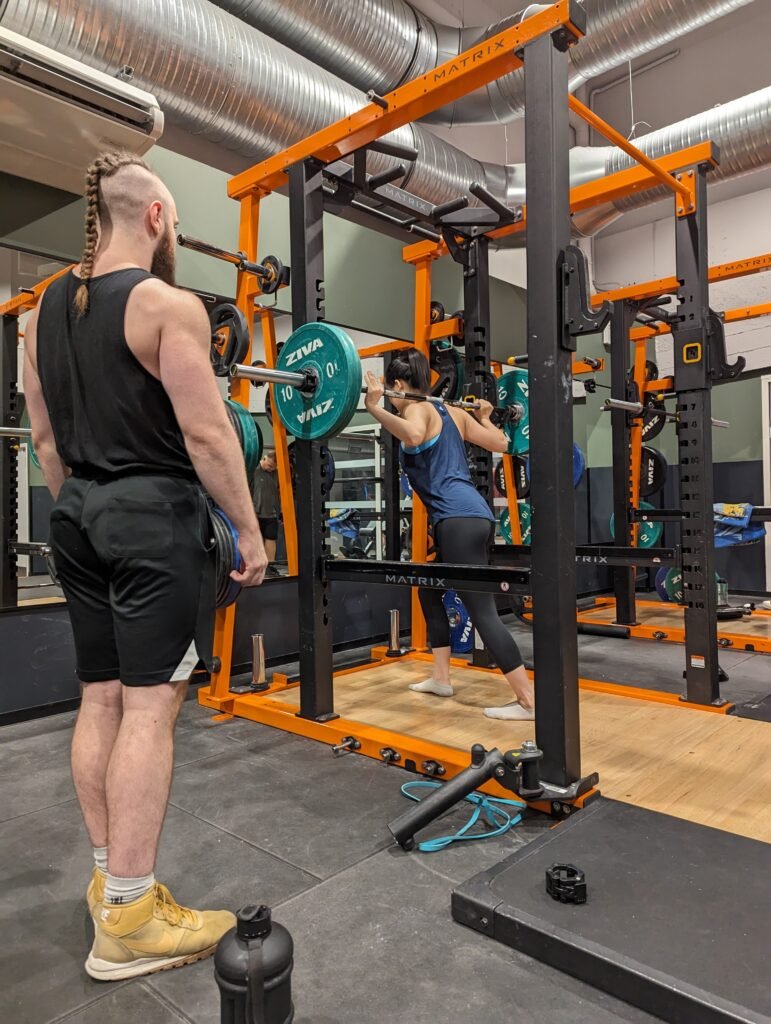 femme s'entraînant sur barre de squat sous supervision d'un coach en salle de sport