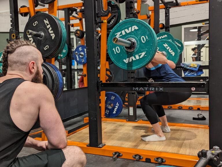 femme s'entraînant sur barre de squat matrix sous supervision d'un coach