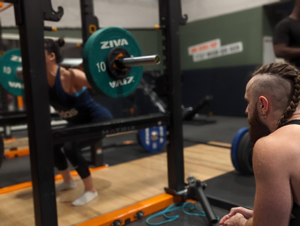femme s'entraînant sur barre de squat sous supervision d'un entraineur sportif