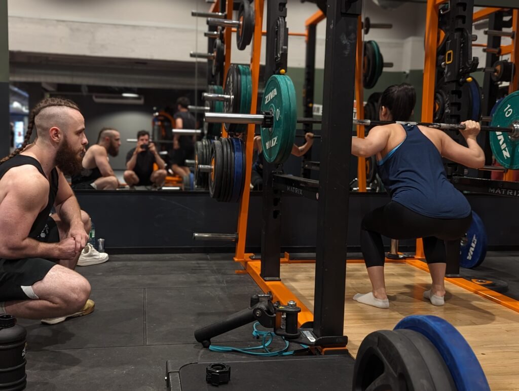 femme s'entraînant sur barre de squat sous supervision d'un coach sportif