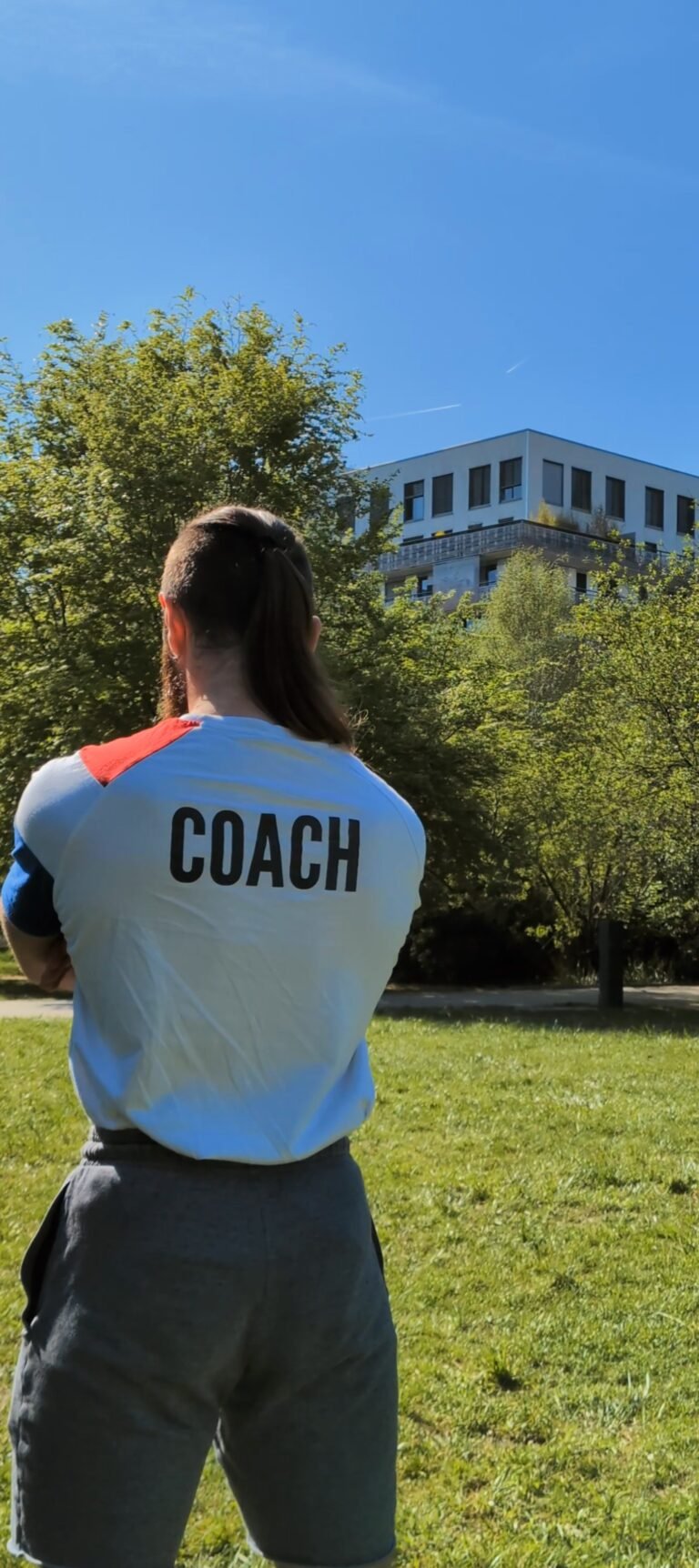 image d'un coach de dos avec un tshirt qui mentionne "coach" dans un parc