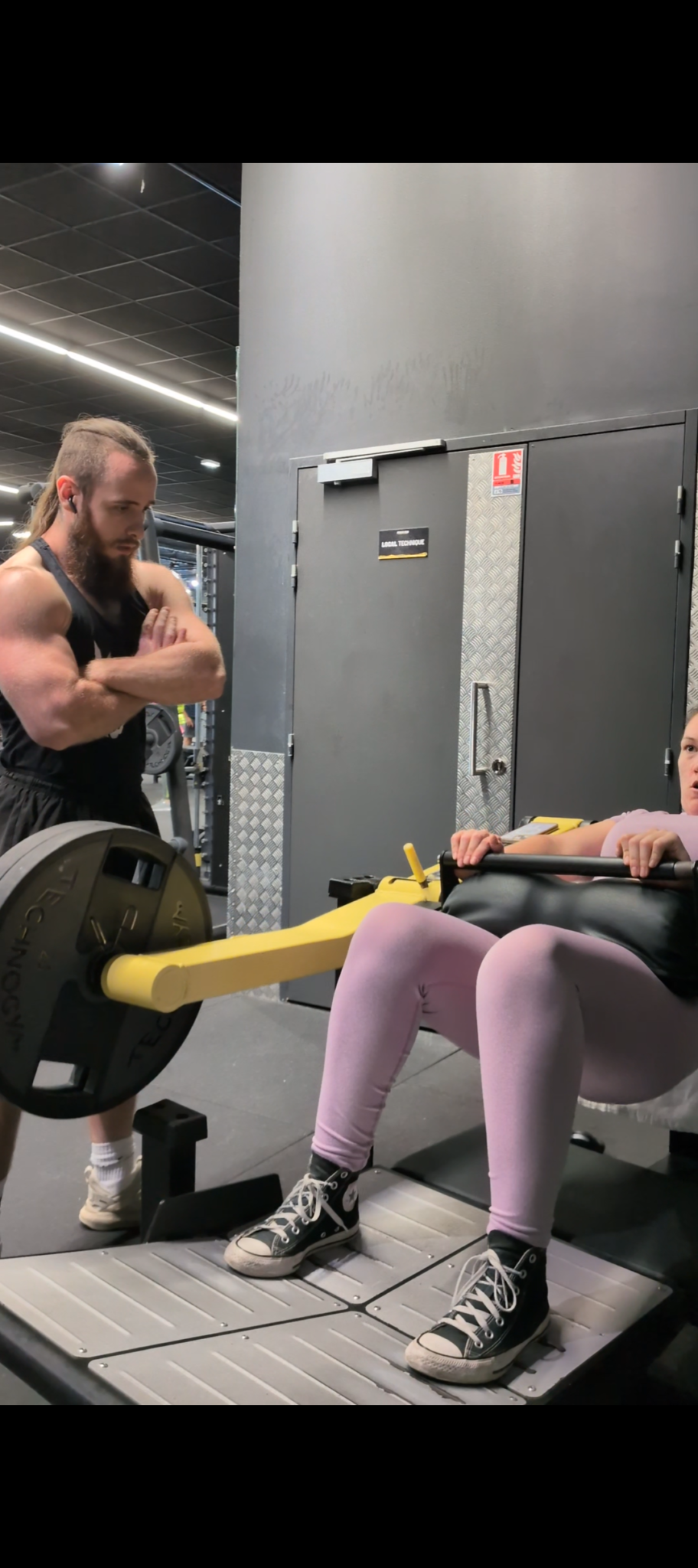 Une femme fait des exercices sur un banc de muscu à la salle de sport avec un entraîneur observant