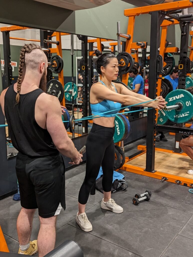 Une femme fait des exercices de résistance à la salle de sport avec un coach sportif qui observe