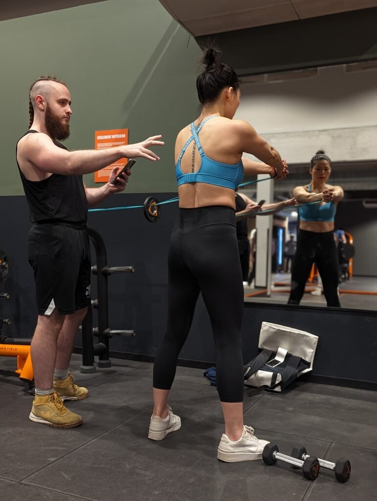 Une femme fait des exercices de résistance devant un miroir à la salle de sport avec un entraîneur observant