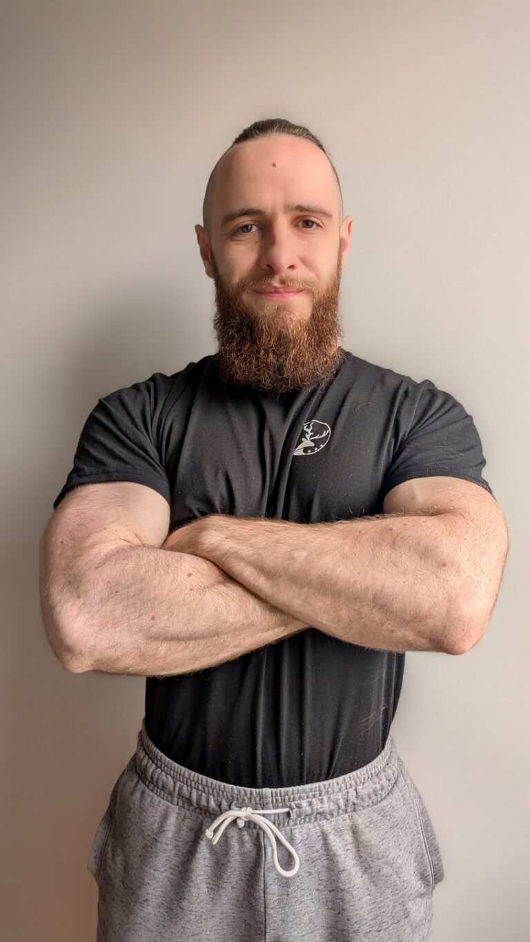 Homme musclé avec une barbe, bras croisés, portant une chemise noire
