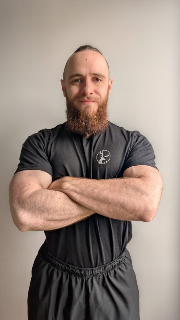 Homme musclé avec barbe portant un t-shirt noir, bras croisés